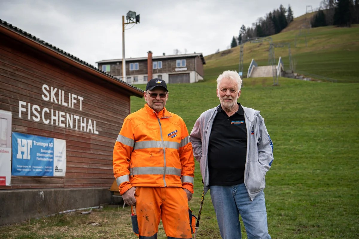 Zwei Männer stehen vor der Talstation des Skilifts Fischenthal. Einer in Jeans, einer in oranger Arbeitskleidung.